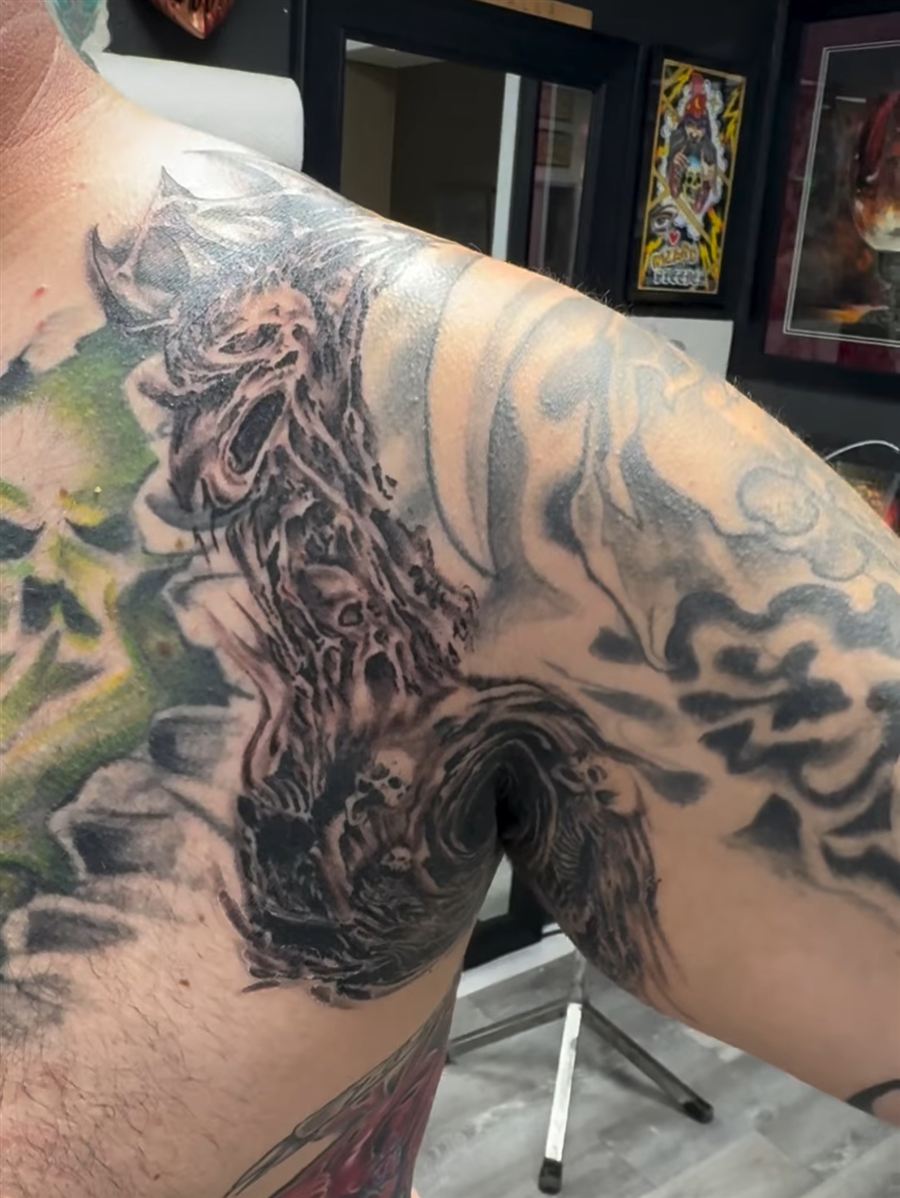 Large black and grey shoulder and chest piece tattoo with green accents