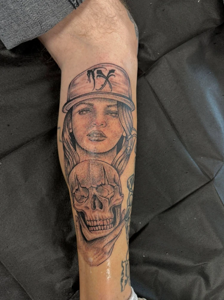 Black and grey portrait of a girl in a TX cap holding a skull, forearm tattoo