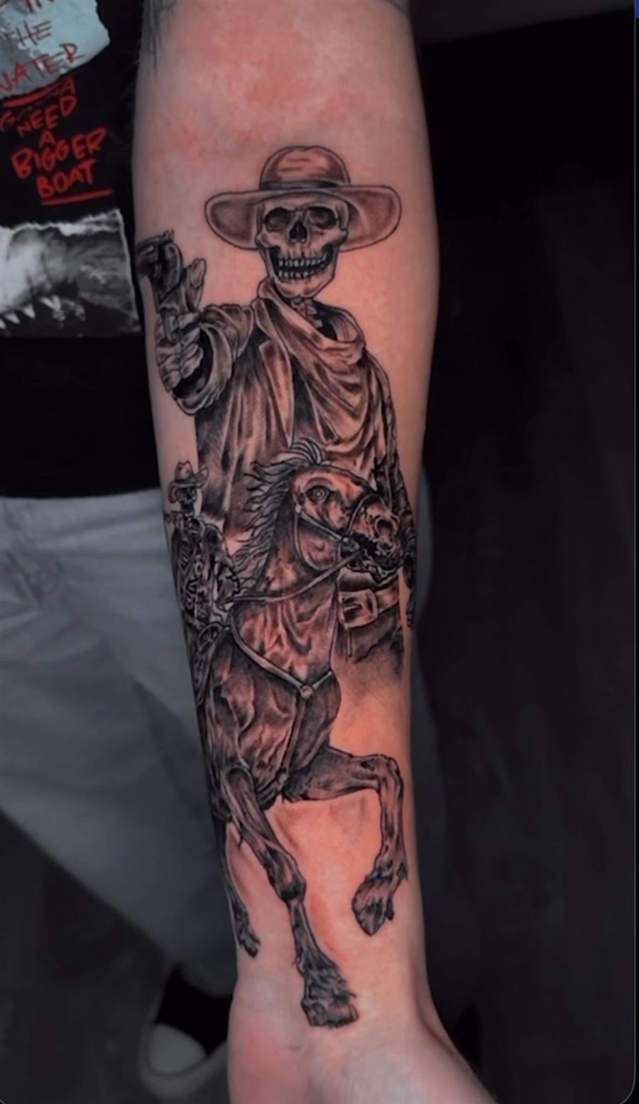 Black and grey forearm sleeve tattoo of a skeleton cowboy riding a skeleton horse